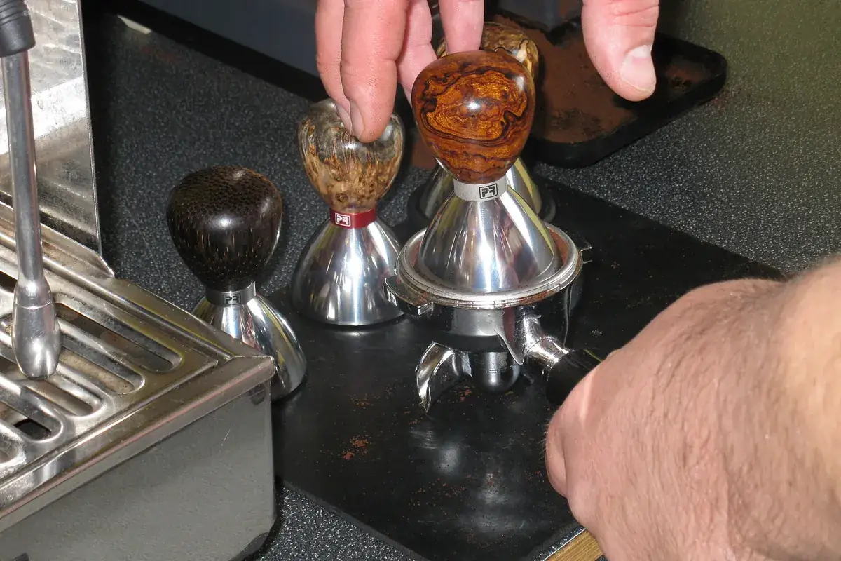 Manos colocando prensadores de café de madera junto a un portafiltros sobre una máquina de espresso