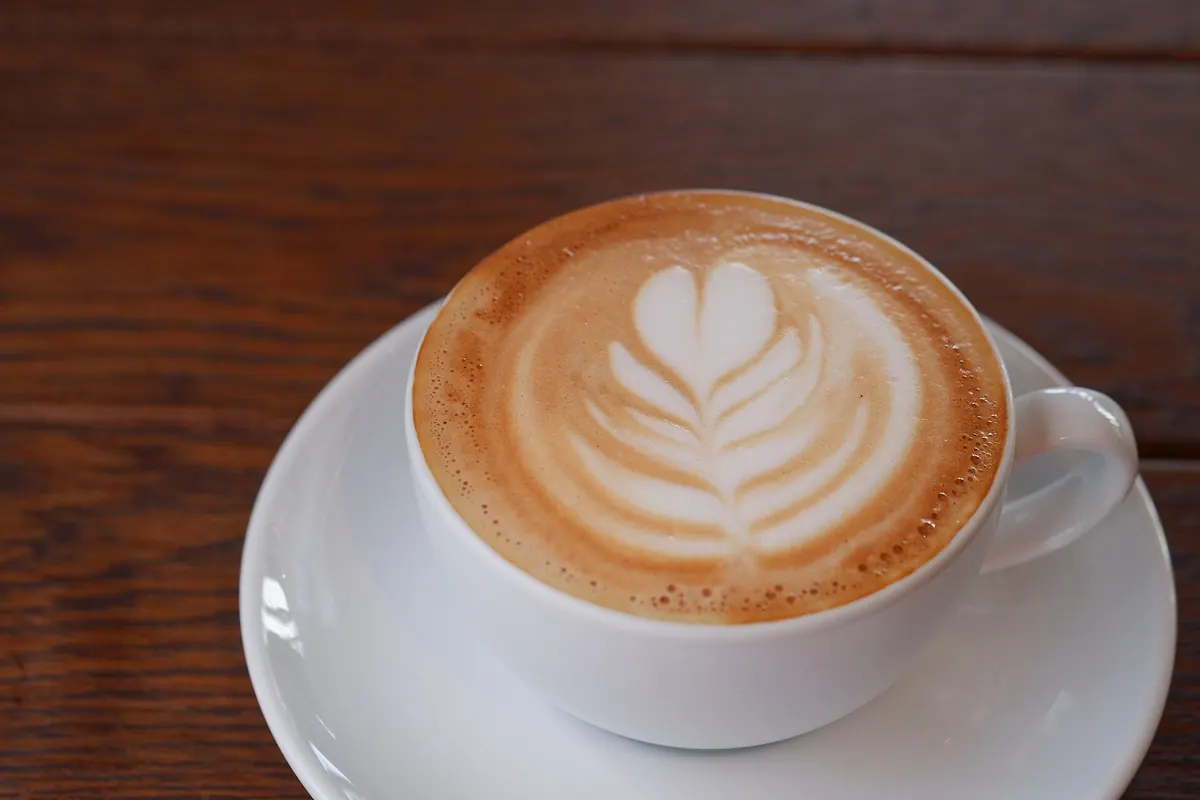 Taza blanca de capuchino con arte latte en forma de hoja sobre mesa de madera