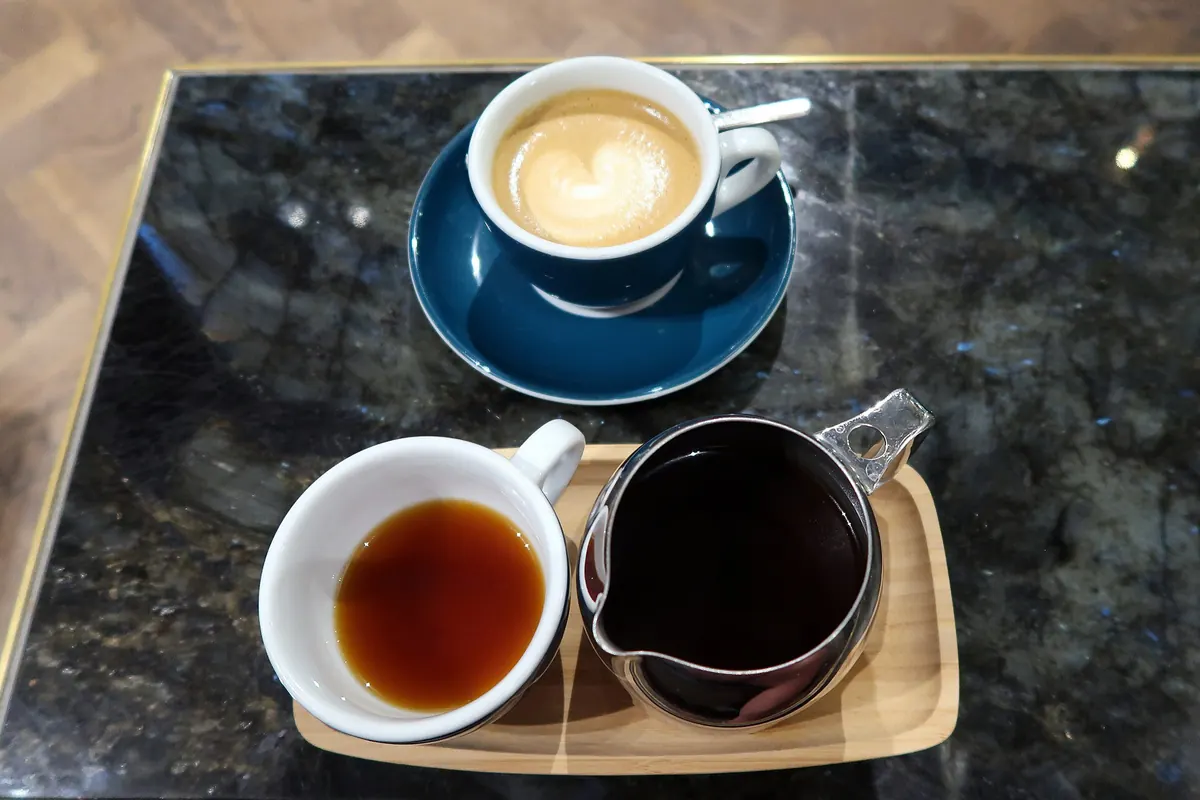 Taza de café con leche y café de filtro servidos sobre una bandeja de madera