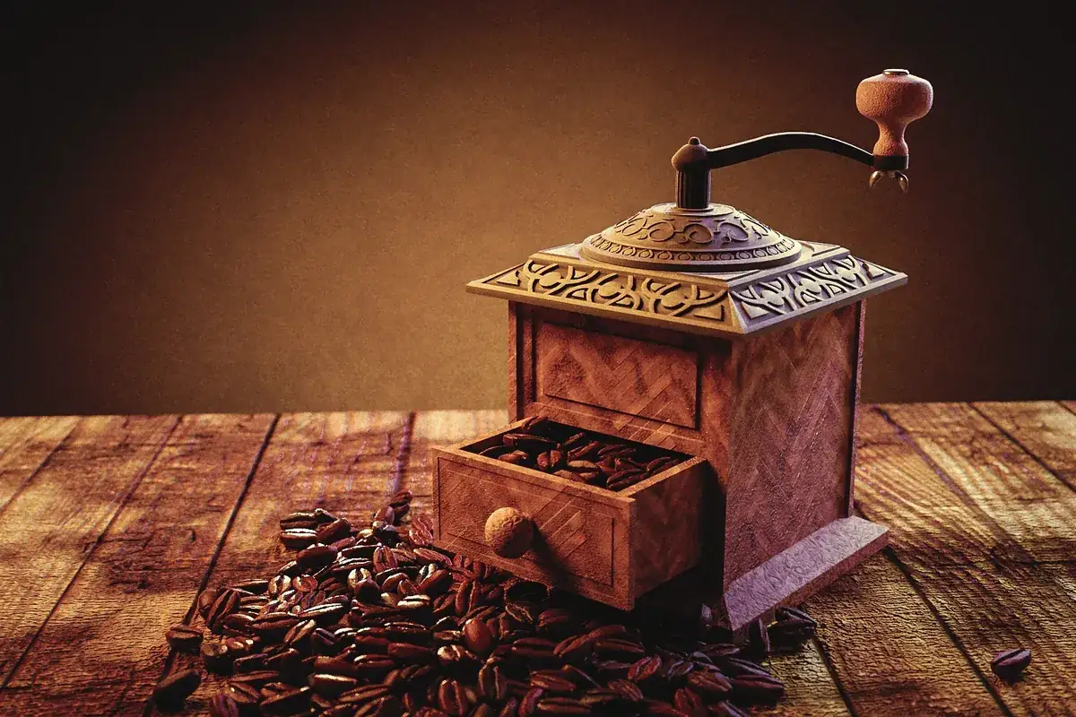 Molinillo de café manual de madera con granos esparcidos sobre una mesa rústica
