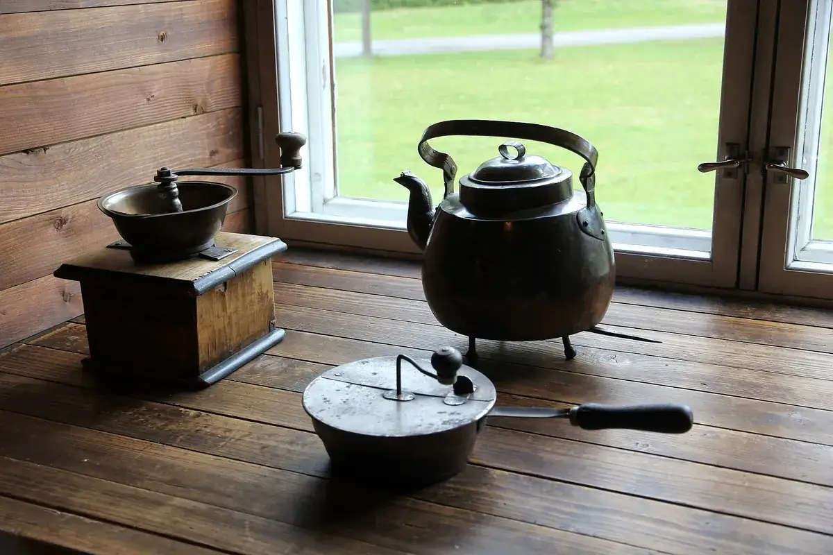 Molinillo manual antiguo y tetera de hierro junto a una ventana en una cabaña de madera