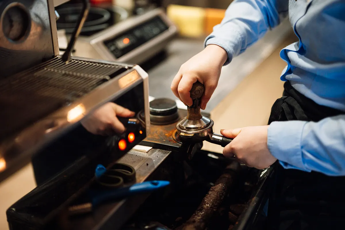 Barista prensando el café en el portafiltros junto a una máquina de espresso